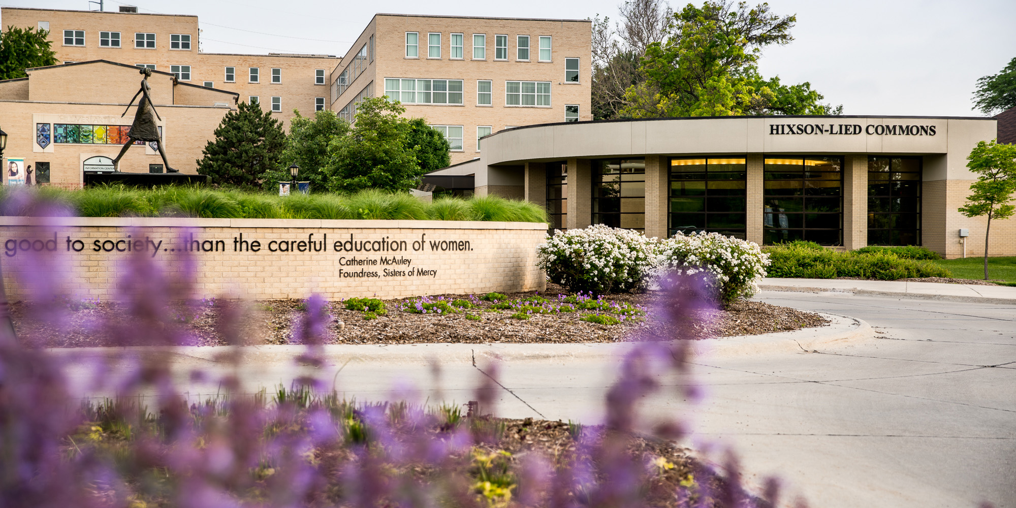 A photo of the College of Saint Mary campus, featuring the Woman Walking statue and the Hixson-Lied Commons buildiong.